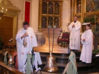 El párroco de la iglesia bendice la nueva campana durante la celebración de una misa vespertina. 